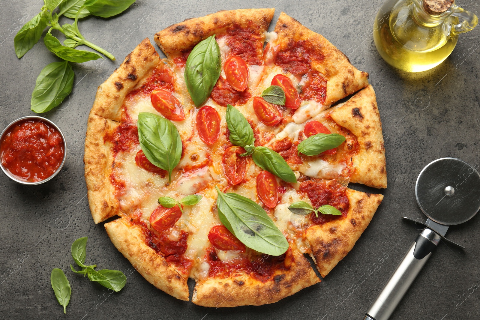 Photo of Delicious Margherita pizza, ingredients and cutter on grey table, top view