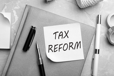 Reminder note with words TAX REFORM and stationery on table, flat lay