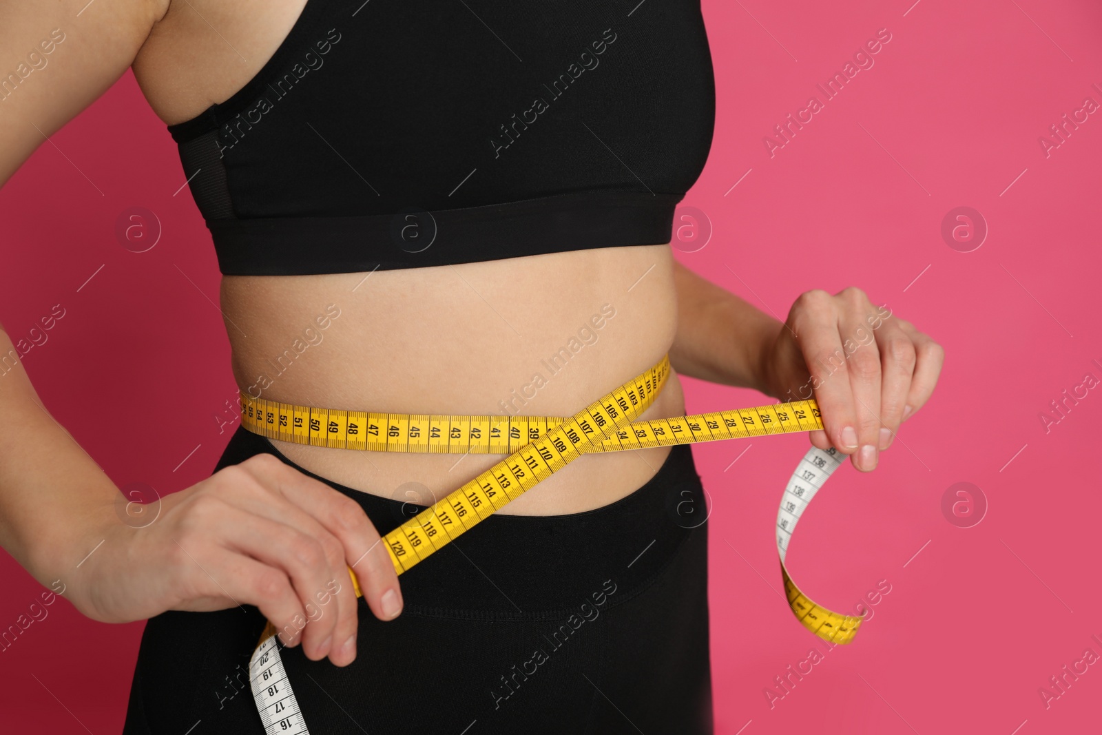 Photo of Woman measuring waist with tape on pink background, closeup