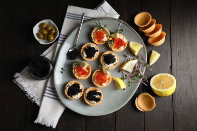 Delicious tartlets with red and black caviar served on wooden table, flat lay