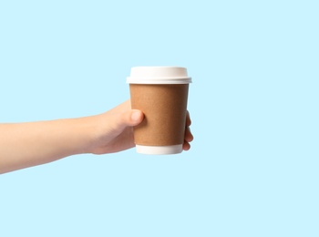 Photo of Woman holding takeaway paper coffee cup on light blue background, closeup