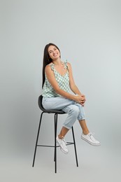 Beautiful young woman sitting on stool against light grey background