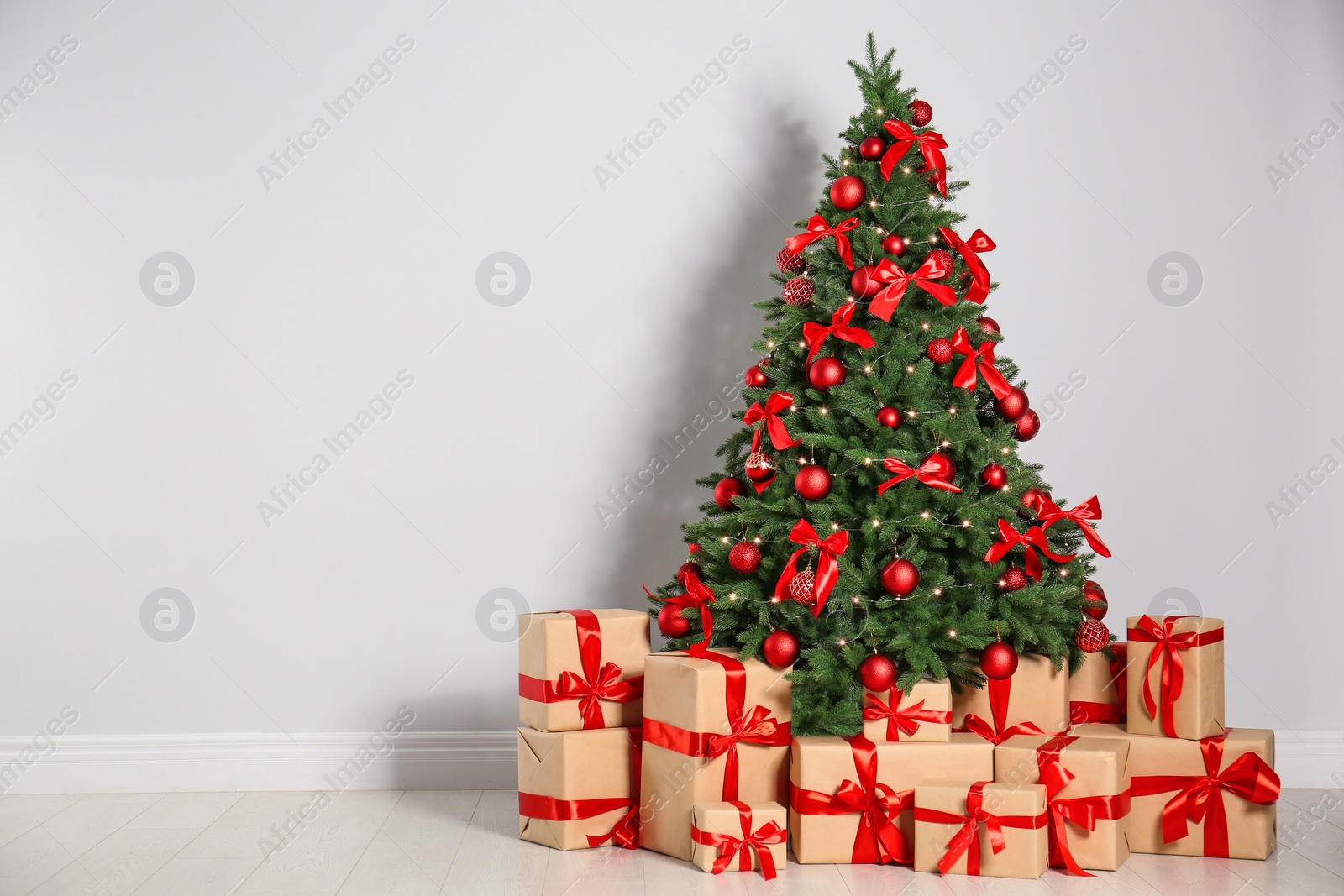 Photo of Decorated Christmas tree and gift boxes near light wall. Space for text