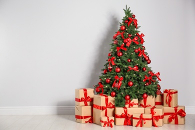 Decorated Christmas tree and gift boxes near light wall. Space for text