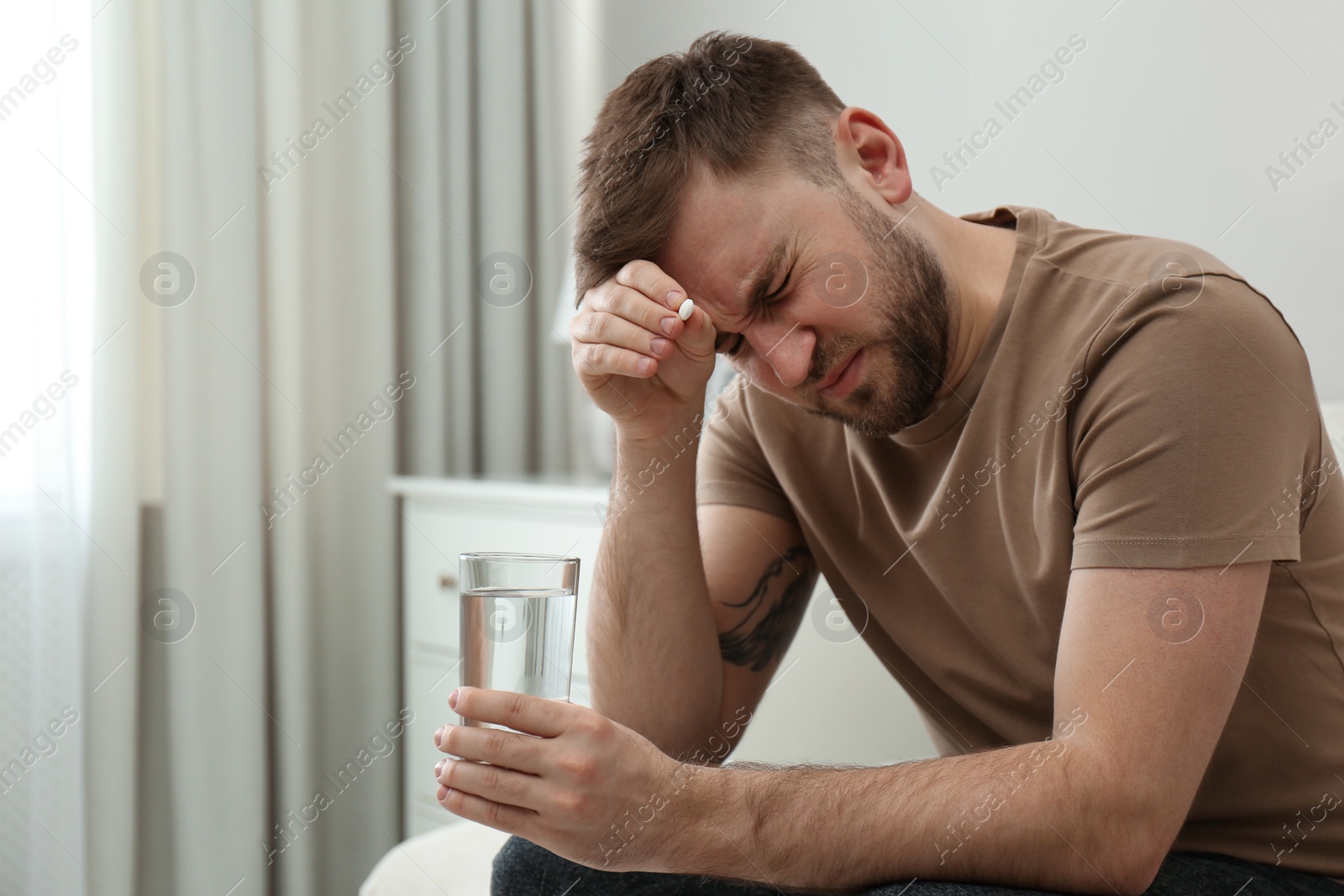 Photo of Man with glass of water and pill suffering from migraine at home