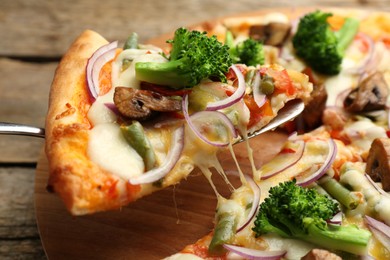 Photo of Taking piece of delicious vegetarian pizza at wooden table, closeup