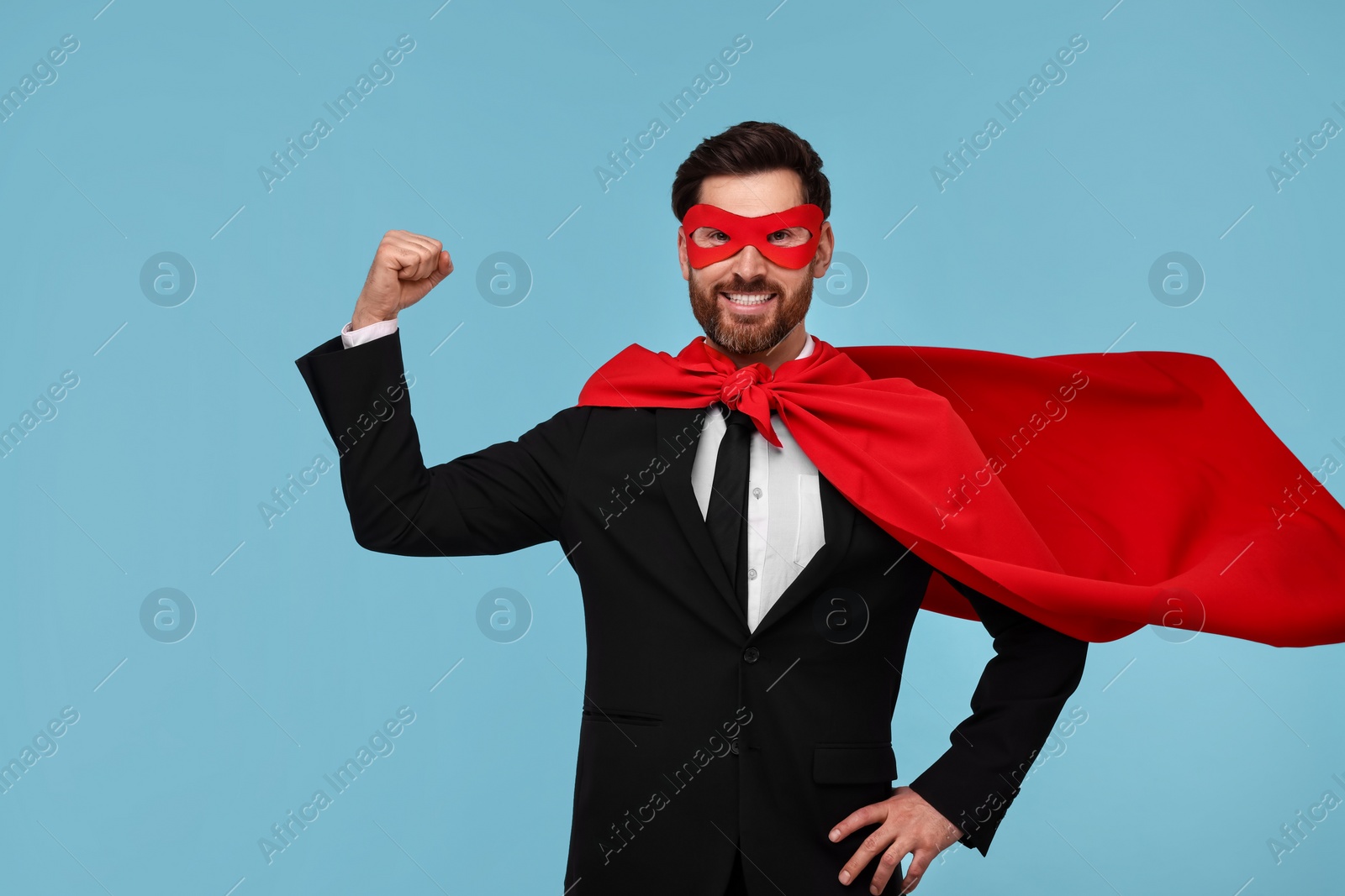 Photo of Businessman wearing red superhero cape and mask on light blue background