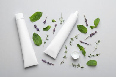 Blank tubes of toothpaste, mint, thyme and lavender flowers on white background, flat lay