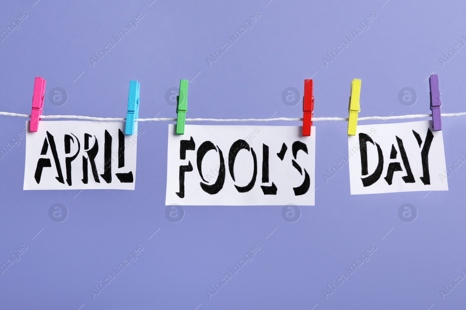 Photo of Words APRIL FOOL'S DAY with pegs on laundry line against violet background