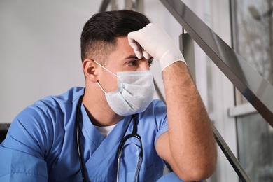 Sad doctor in facial mask indoors. Stress of health care workers during coronavirus pandemic