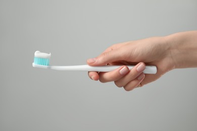 Photo of Woman holding toothbrush with paste on light grey background, closeup