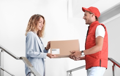 Photo of Young woman receiving parcel from courier indoors