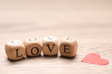 Photo of Mini cubes with letters forming word Love near red paper heart on wooden background, closeup