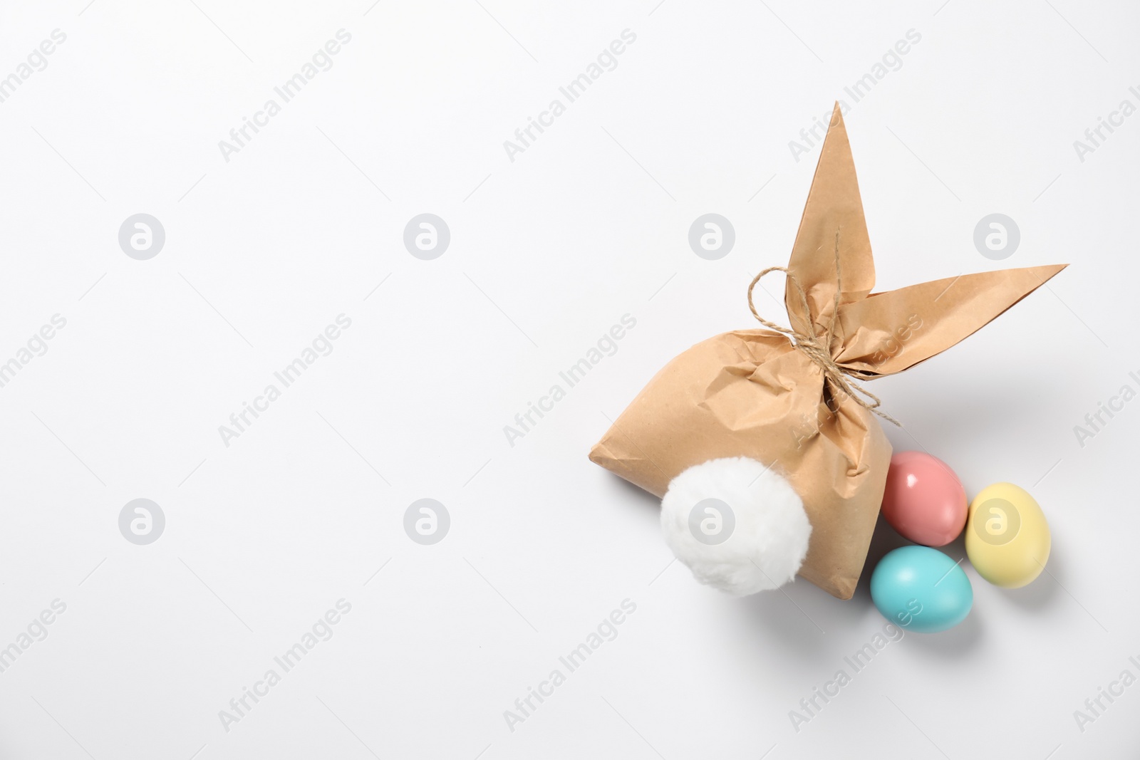 Photo of Easter bunny gift bag and dyed eggs on white background, top view