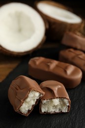 Photo of Delicious milk chocolate candy bars with coconut filling on slate plate, closeup