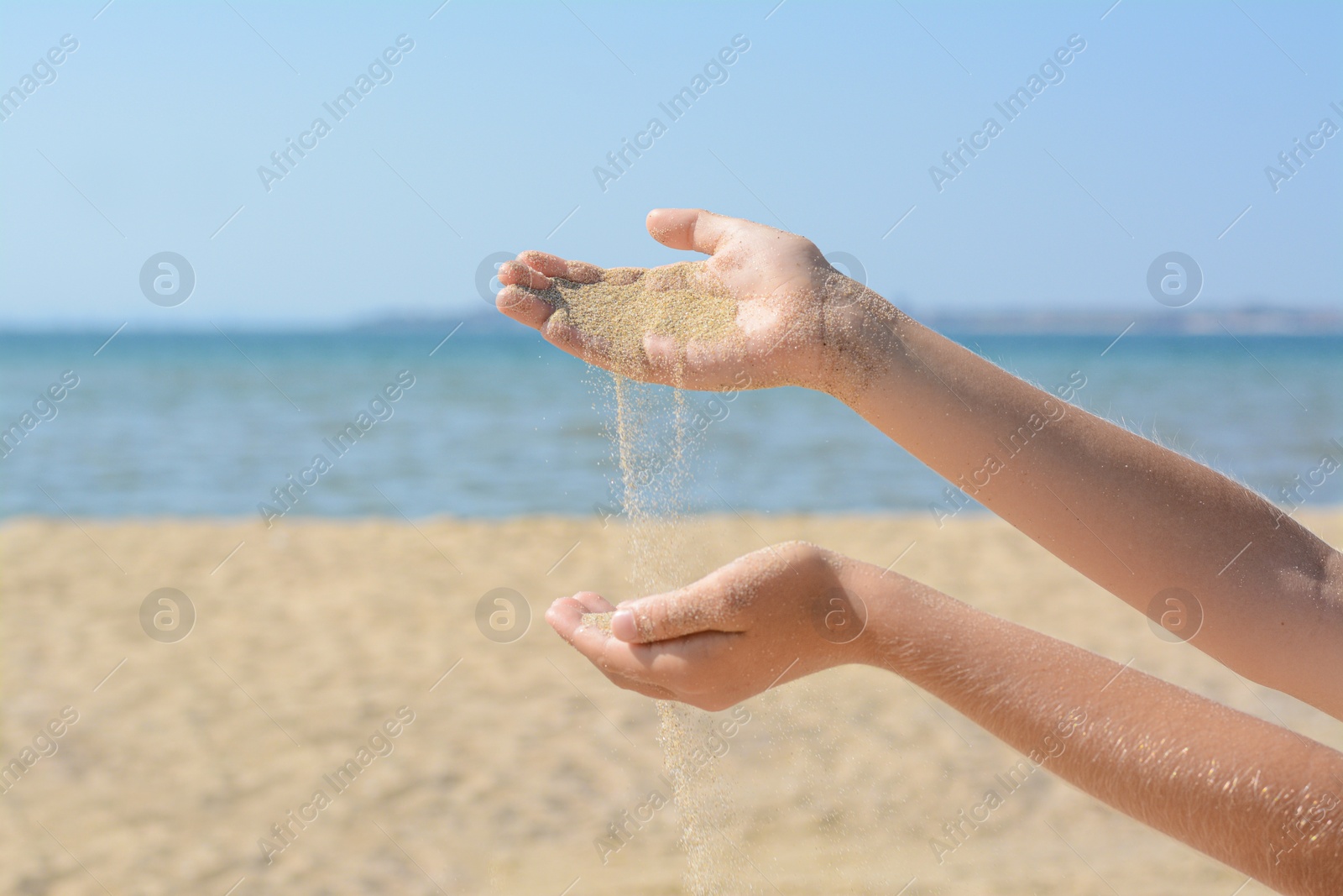 Photo of Child pouring sand from hands on beach, closeup. Fleeting time concept