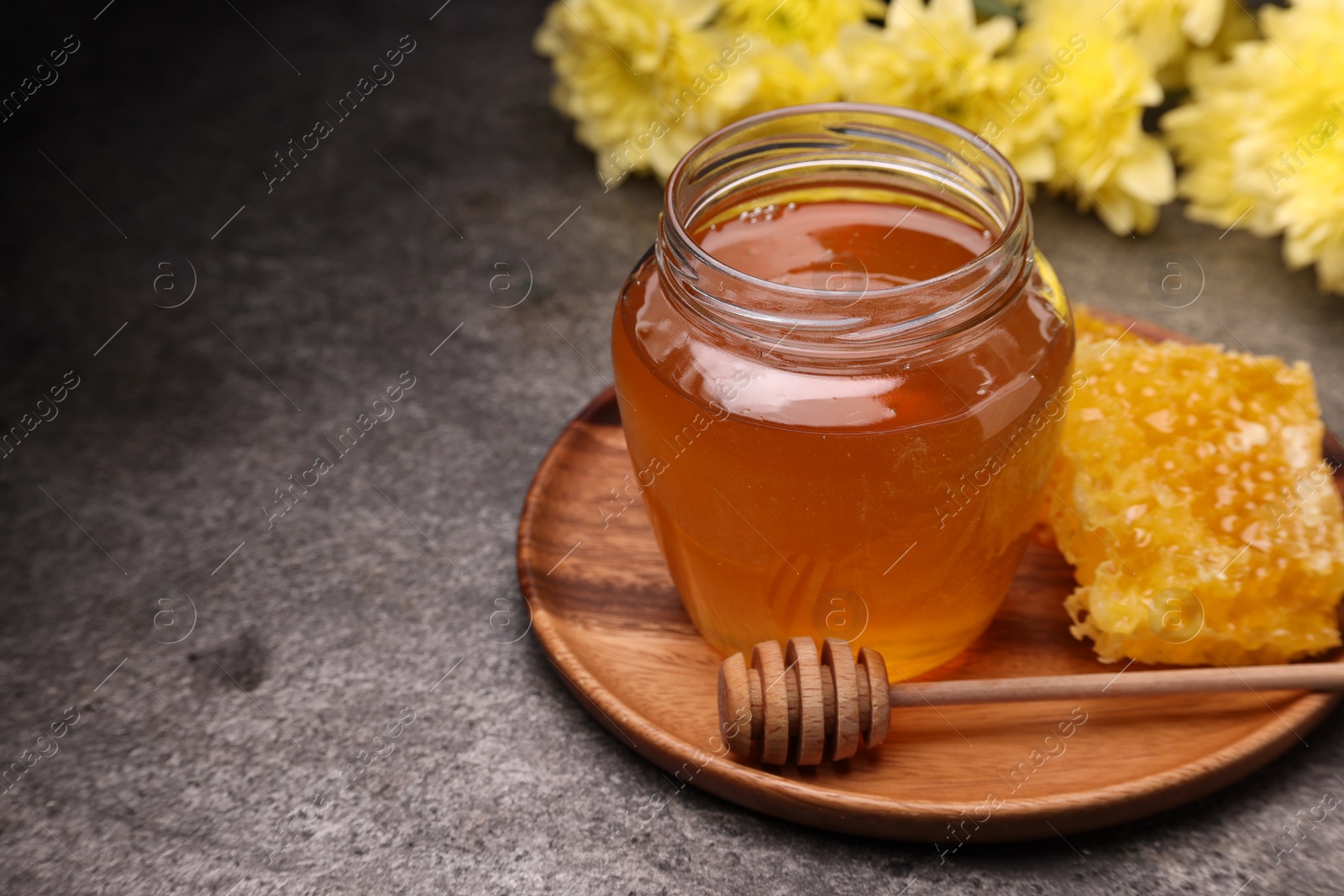Photo of Sweet golden honey in jar, dipper and honeycomb on grey textured table, space for text