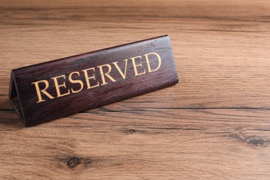 Photo of Elegant sign RESERVED on wooden surface, space for text. Table setting element