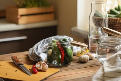 Glass jar with fresh cucumbers and other ingredients on wooden table indoors. Pickling vegetables