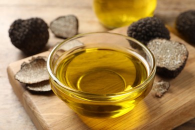Photo of Glass bowl of truffle oil with wooden board on table, closeup