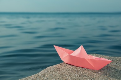 Photo of Pink paper boat near river on sunny day, space for text