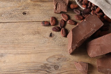 Photo of Pieces of tasty milk chocolate and cocoa beans on wooden table, flat lay. Space for text