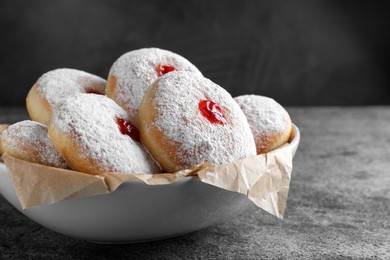 Photo of Delicious donuts with jelly and powdered sugar in bowl on grey table