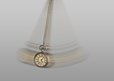 Image of Hypnosis session. Vintage pocket watch with chain swinging on light background, motion effect
