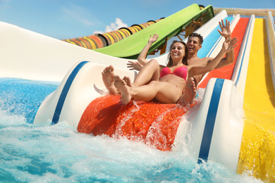 Photo of Happy couple on slide at water park, low angle view. Summer vacation