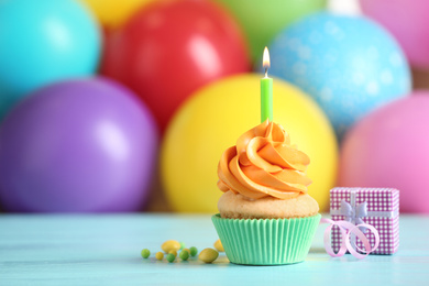 Photo of Delicious birthday cupcake with burning candle and gift on light blue wooden table. Space for text