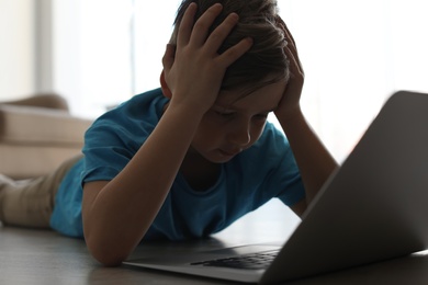 Photo of Upset little child with laptop on floor indoors. Danger of internet