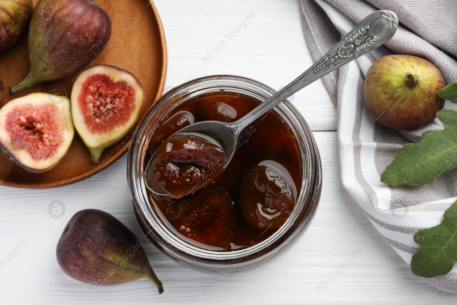 Photo of Jar of tasty sweet jam and fresh figs on white wooden table, flat lay