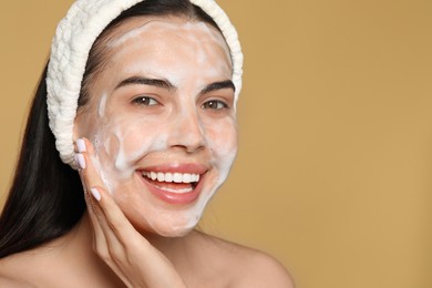 Happy young woman washing face with cosmetic product on beige background, closeup. Space for text