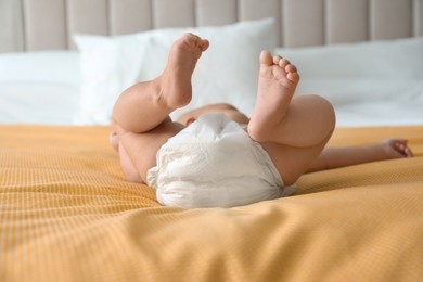 Photo of Cute little baby in diaper on yellow blanket at home, closeup