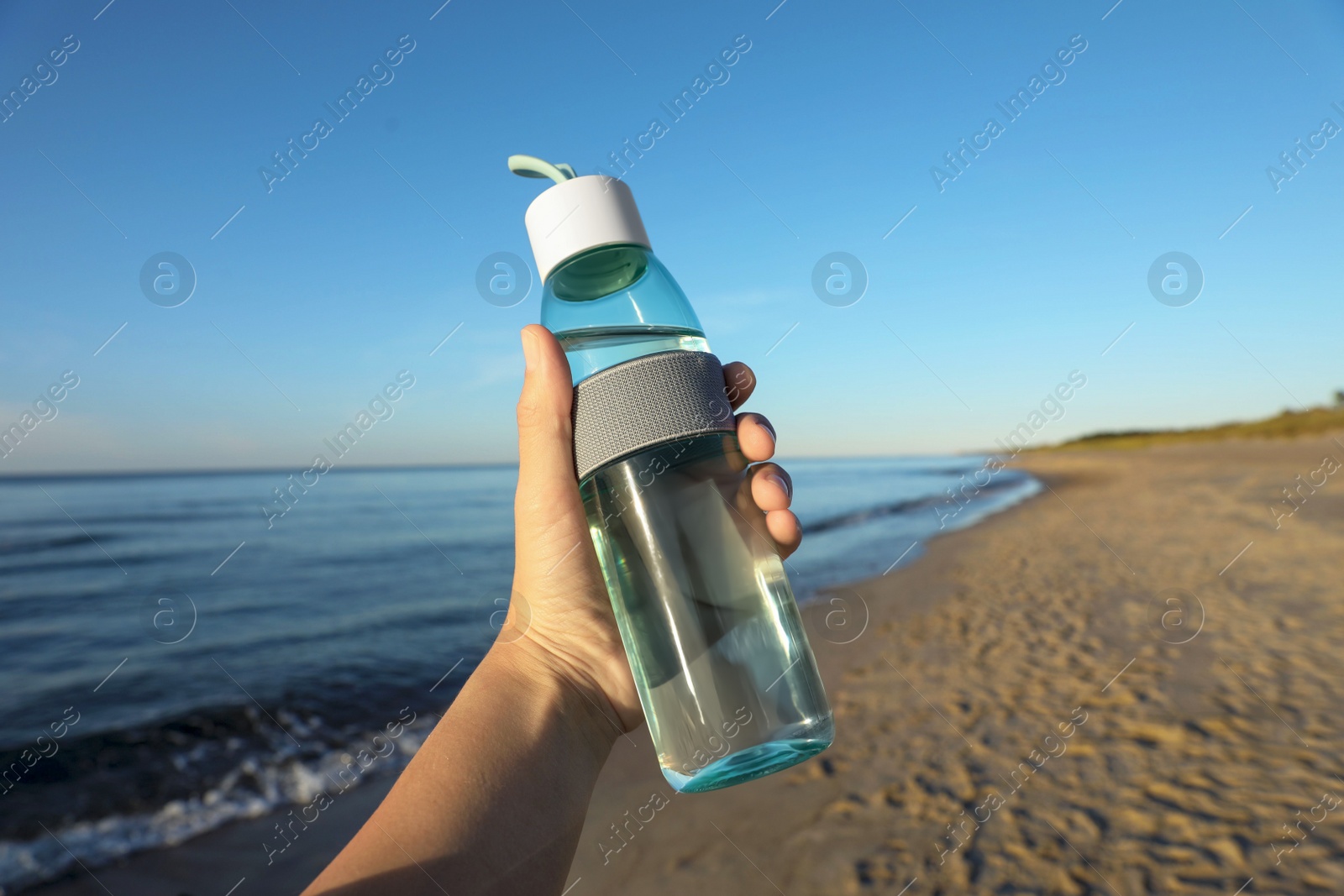 Photo of Woman holding glass bottle with water near sea, closeup