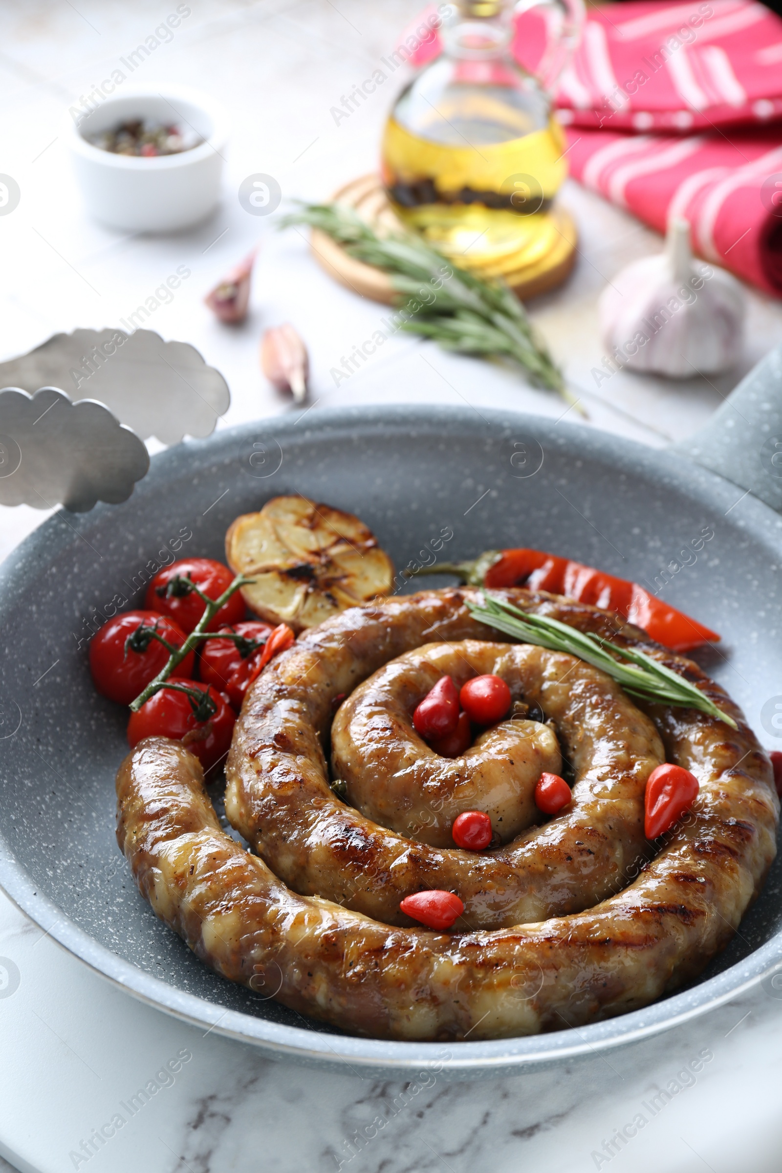 Photo of Delicious homemade sausage with garlic, tomatoes, rosemary and chili in frying pan served on light tiled table, closeup