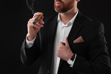 Man in elegant suit smoking cigar on black background, closeup