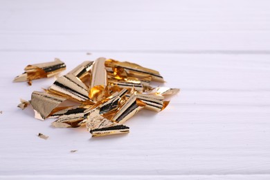 Photo of Many pieces of edible gold leaf on white wooden table, closeup. Space for text