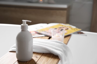 Wooden bath tray with shower gel, candle and fresh towel on tub indoors. Space for text