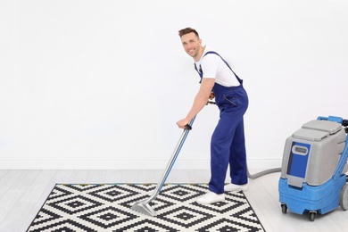 Photo of Male worker removing dirt from carpet with professional vacuum cleaner indoors