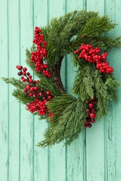 Beautiful Christmas wreath with red berries hanging on turquoise wooden wall