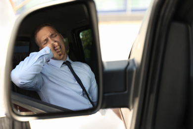 Tired young man yawning in his auto, view through car side mirror