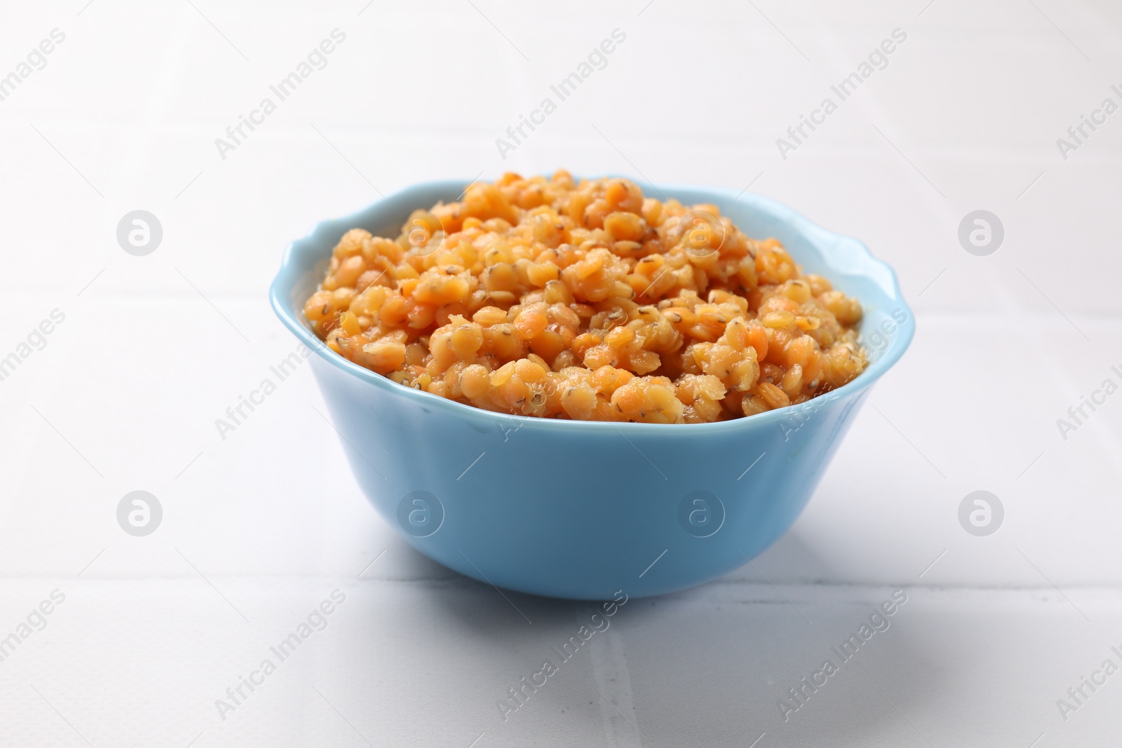 Photo of Delicious red lentils in bowl on white tiled table, closeup