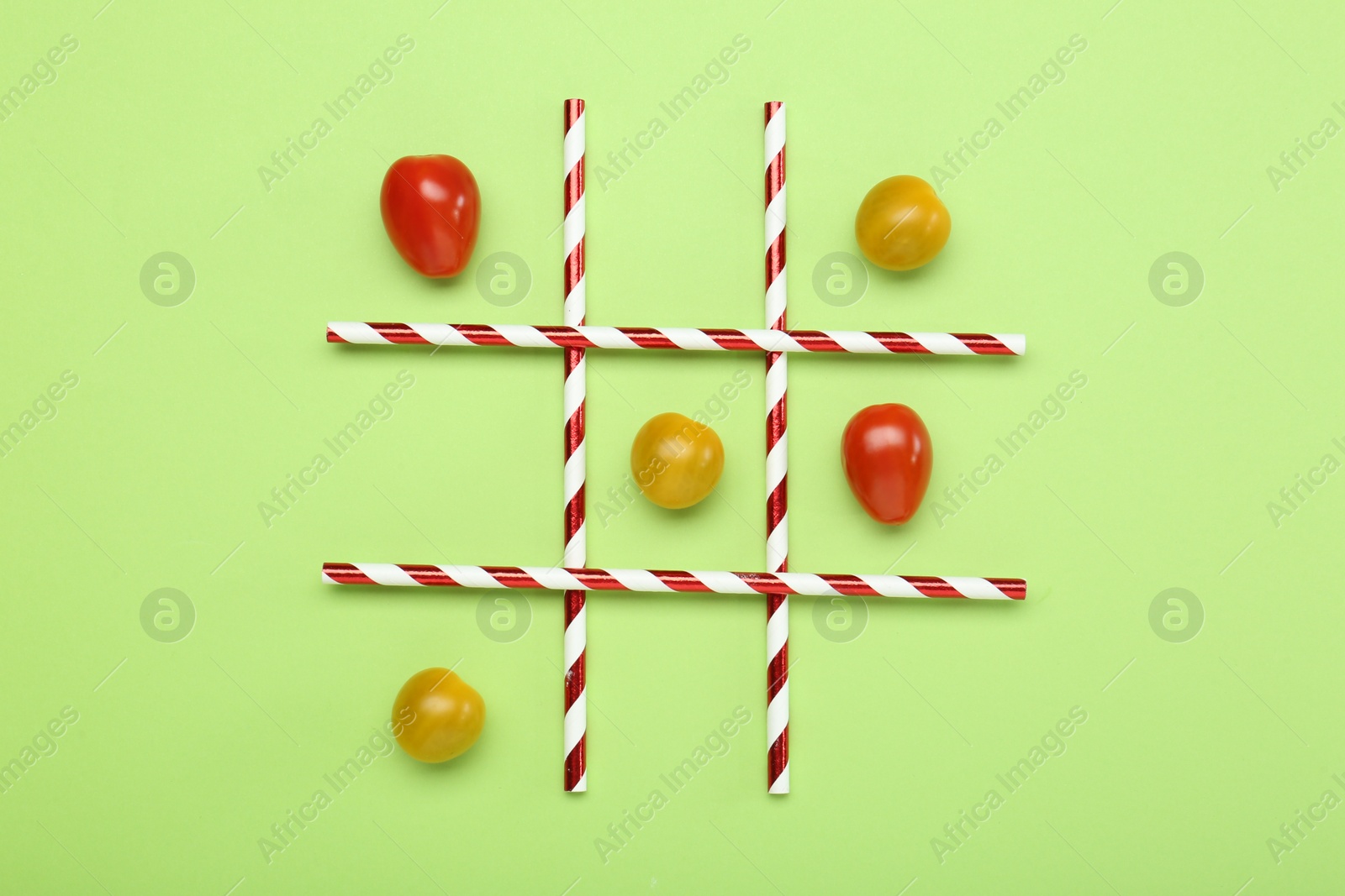 Photo of Tic tac toe game made with cherry tomatoes on light green background, top view