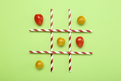 Photo of Tic tac toe game made with cherry tomatoes on light green background, top view