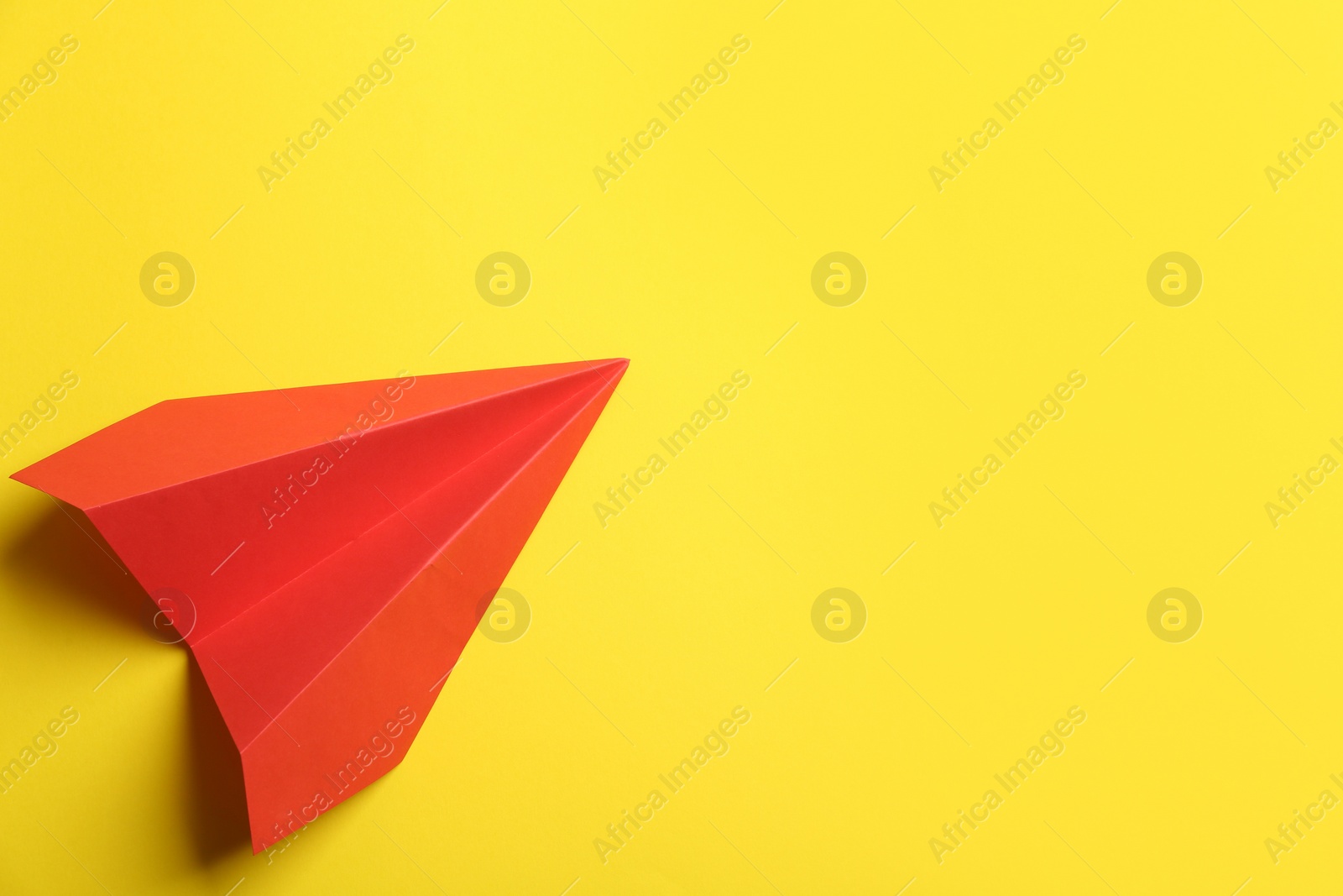 Photo of Red paper plane on yellow background, top view. Space for text