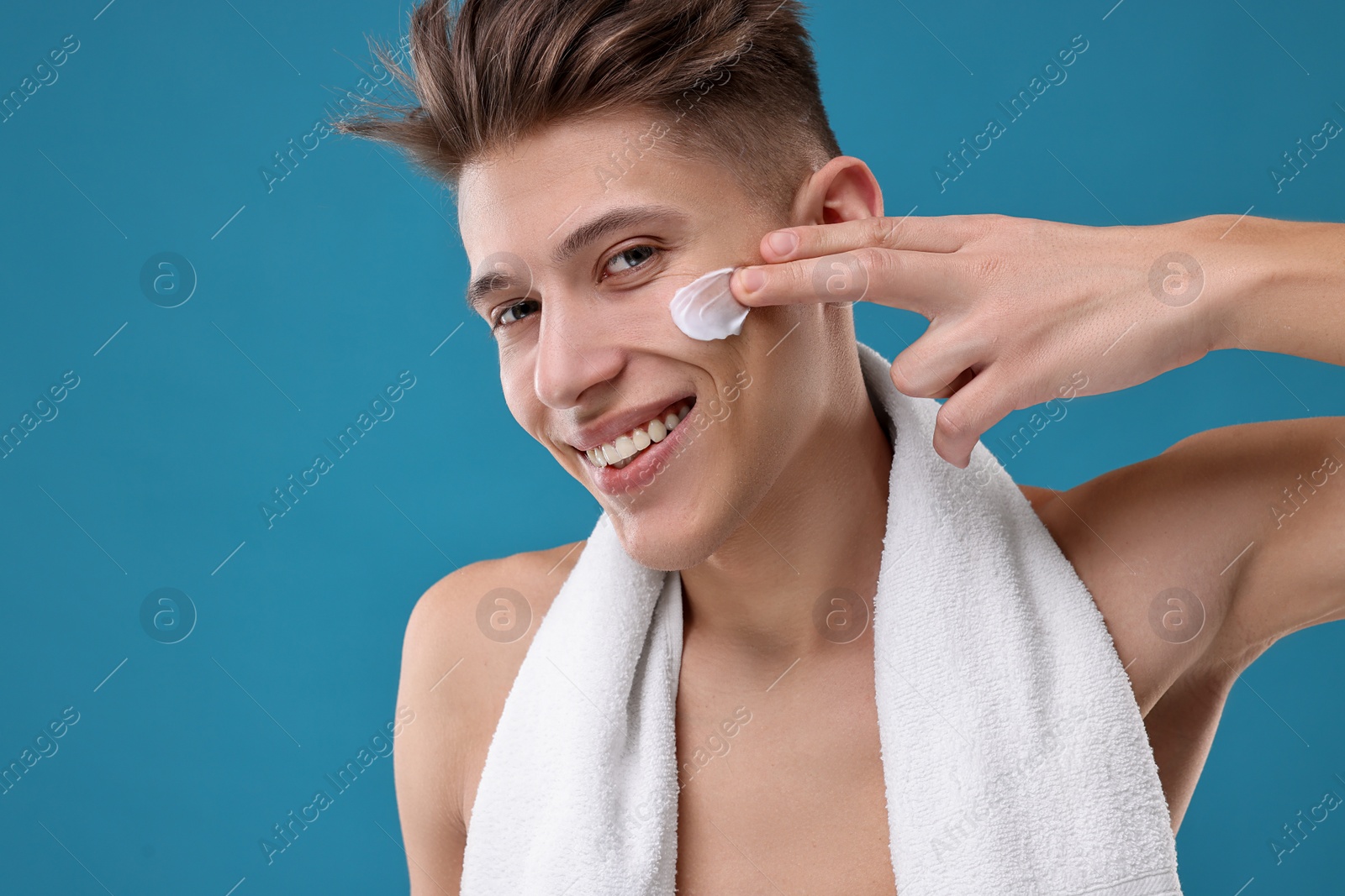 Photo of Handsome man applying moisturizing cream onto his face on blue background