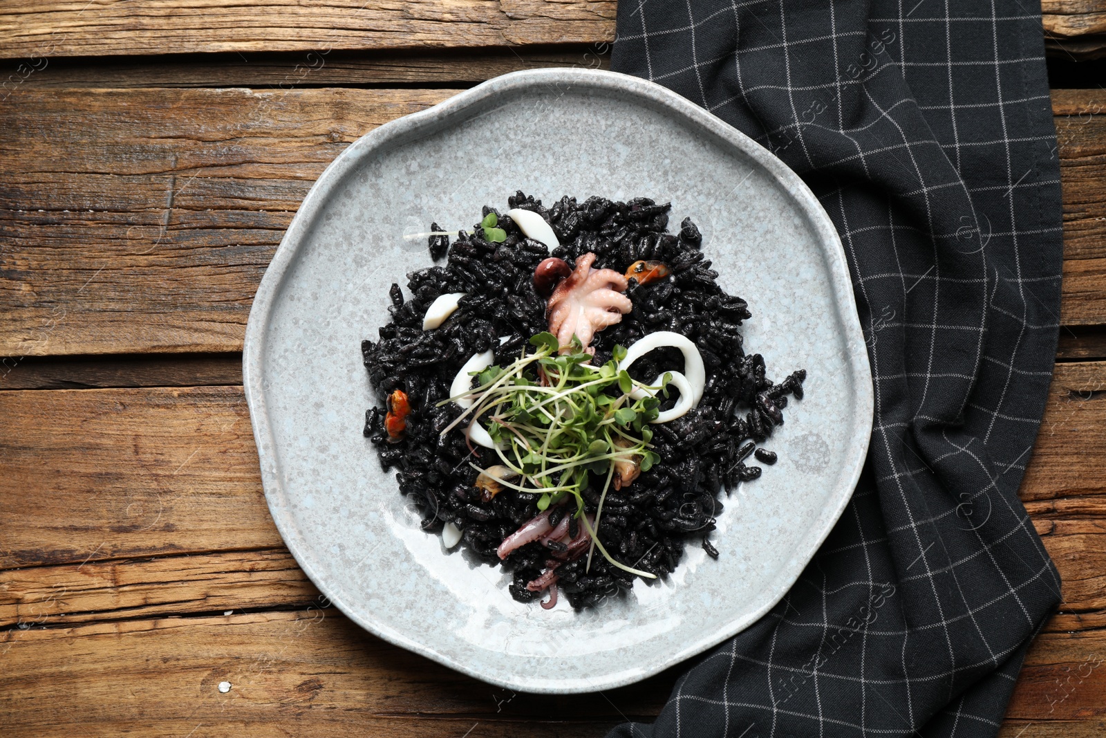 Photo of Delicious black risotto with seafood on wooden table, top view