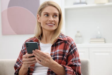 Photo of Happy woman sending message via smartphone at home