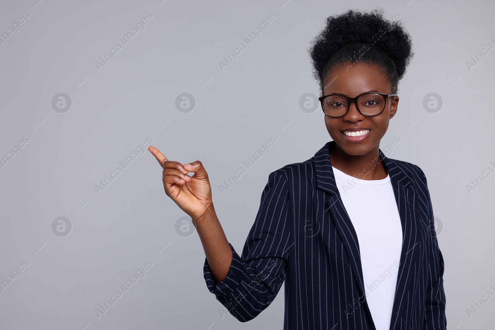 Photo of Beautiful young woman pointing at something on light grey background. Space for text